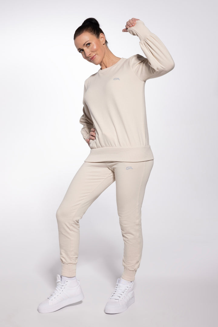 Woman wearing a beige tracksuit with white sneakers on a white background
