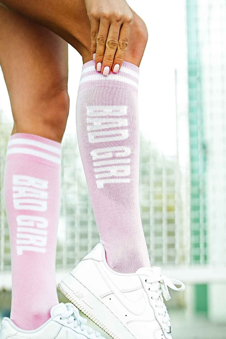 Close-up of powder pink "Bad Girl" knee socks – bold lettering detail on soft cotton fabric
