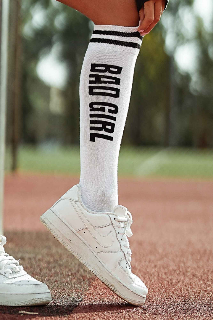 Close-up of white and black "Bad Girl" knee socks – bold lettering detail on soft cotton fabric
