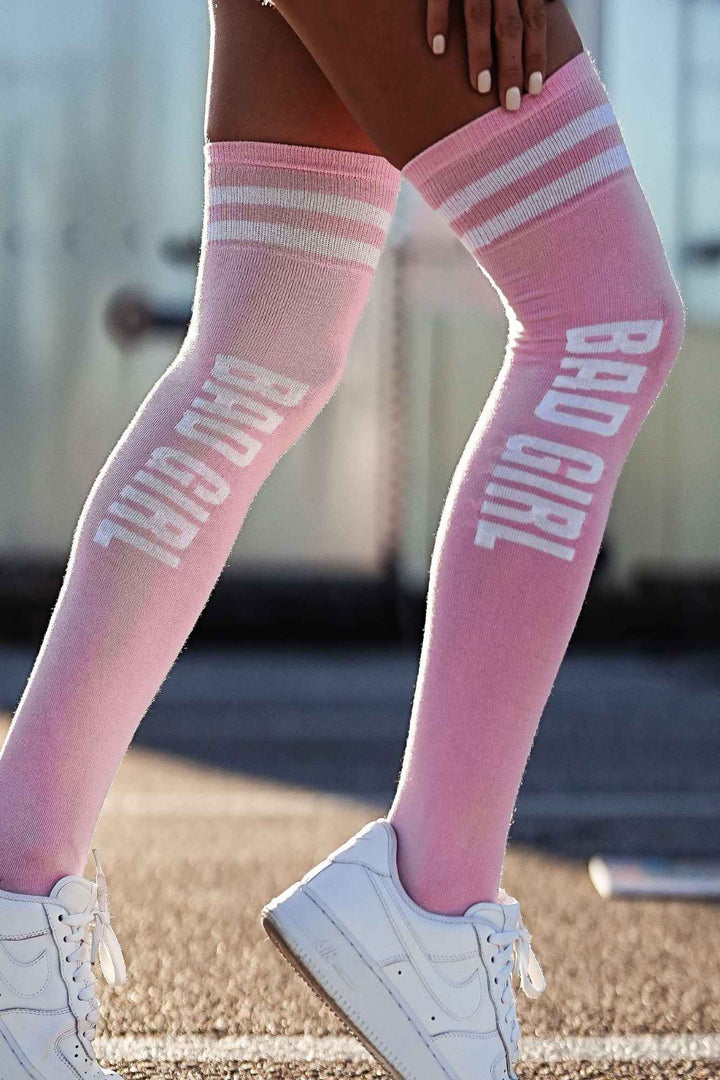 Close-up of powder pink "Bad Girl" over-knee socks – bold lettering detail on soft cotton fabric
