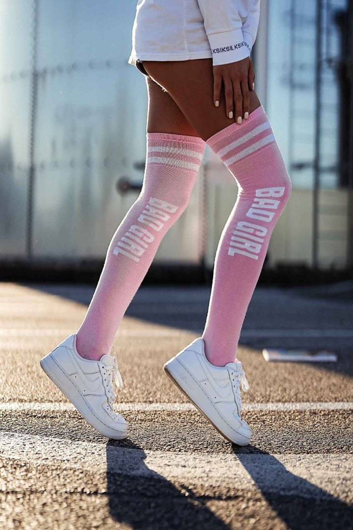 Powder pink "Bad Girl" cotton over-knee socks – side view showing slogan print and full length
