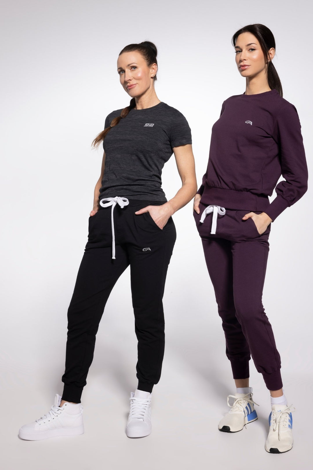 Two women wearing black and purple tracksuits on a white background