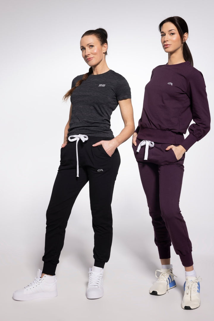 Two women wearing black and purple tracksuits on a white background