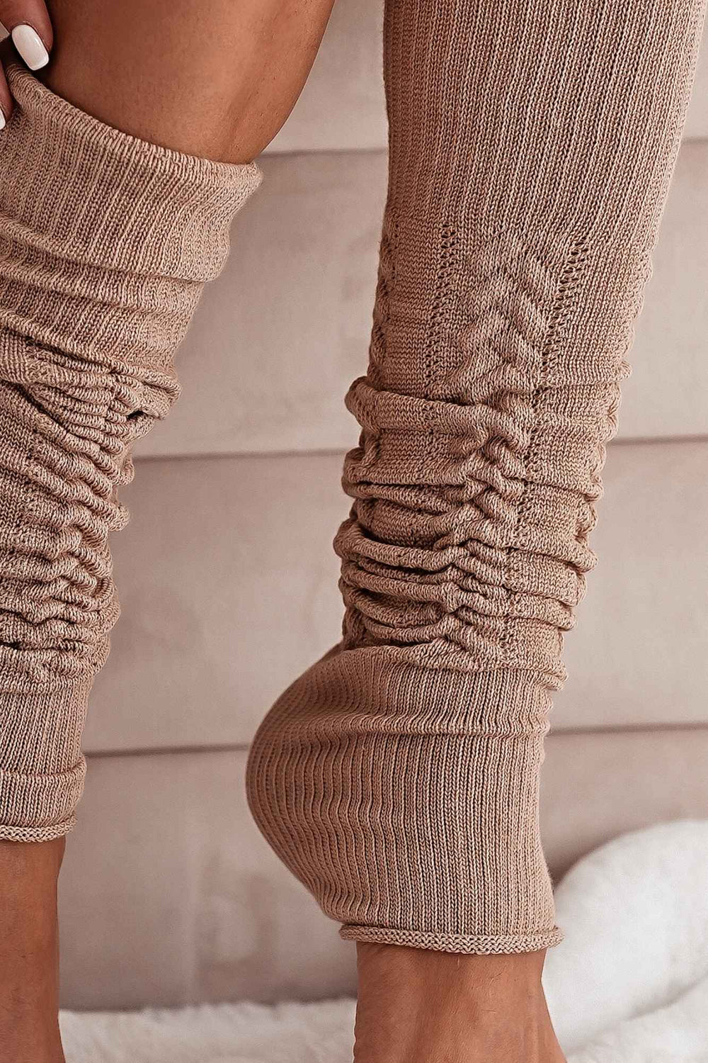 Close-up of beige openwork leg warmers – intricate cotton knit pattern and soft fabric finish
