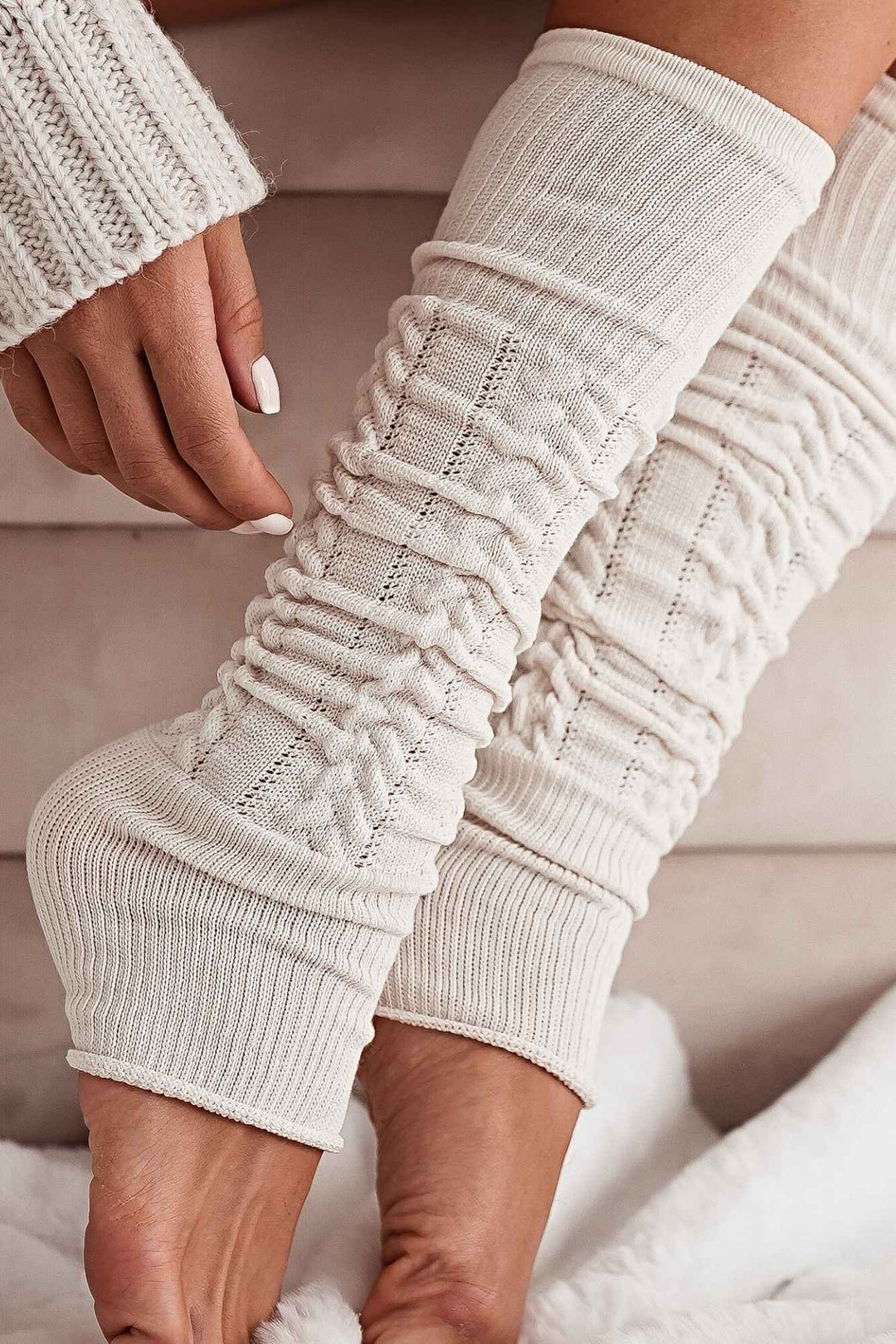 Close-up of ecru openwork leg warmers – intricate cotton knit pattern and soft fabric finish
