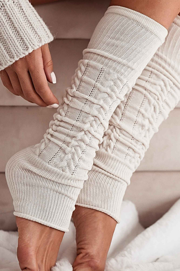 Close-up of ecru openwork leg warmers – intricate cotton knit pattern and soft fabric finish
