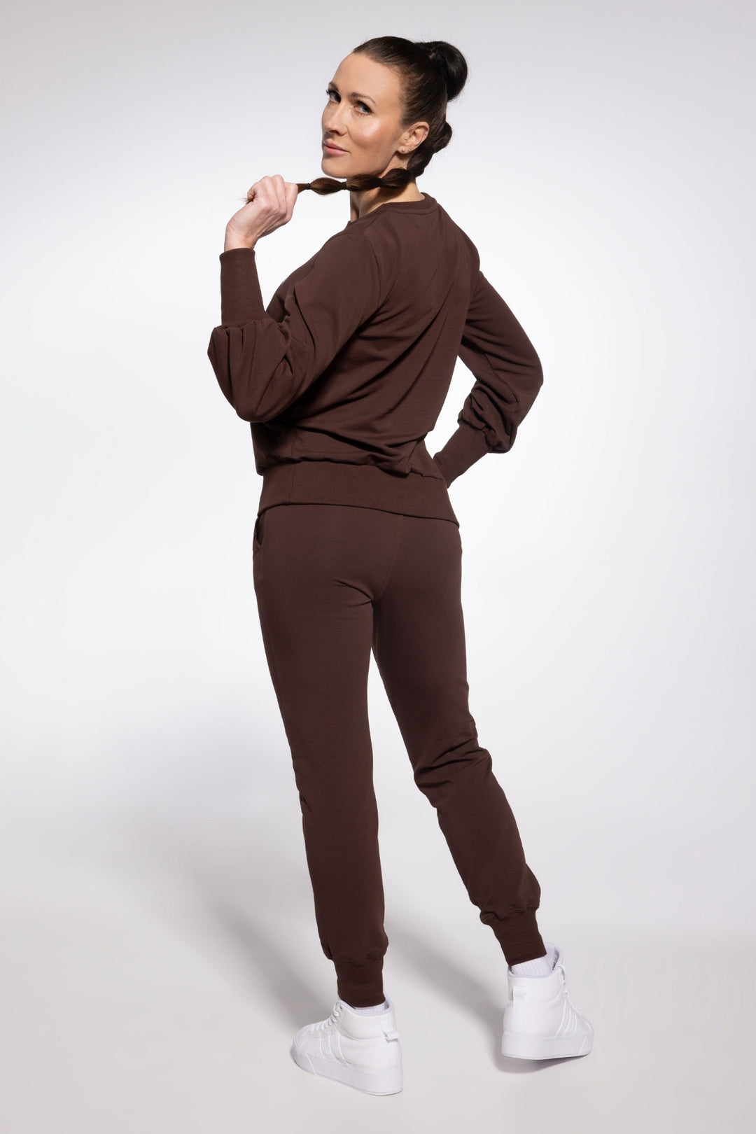 Woman wearing a brown tracksuit with white sneakers on a light gray background