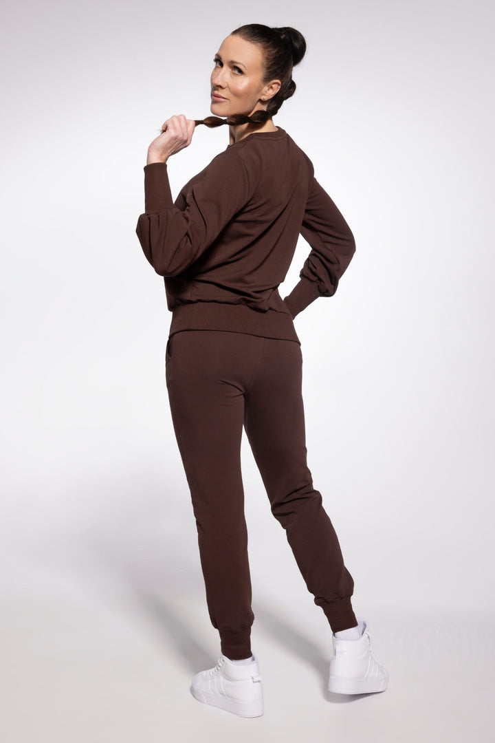 Woman wearing a brown tracksuit with white sneakers on a light gray background