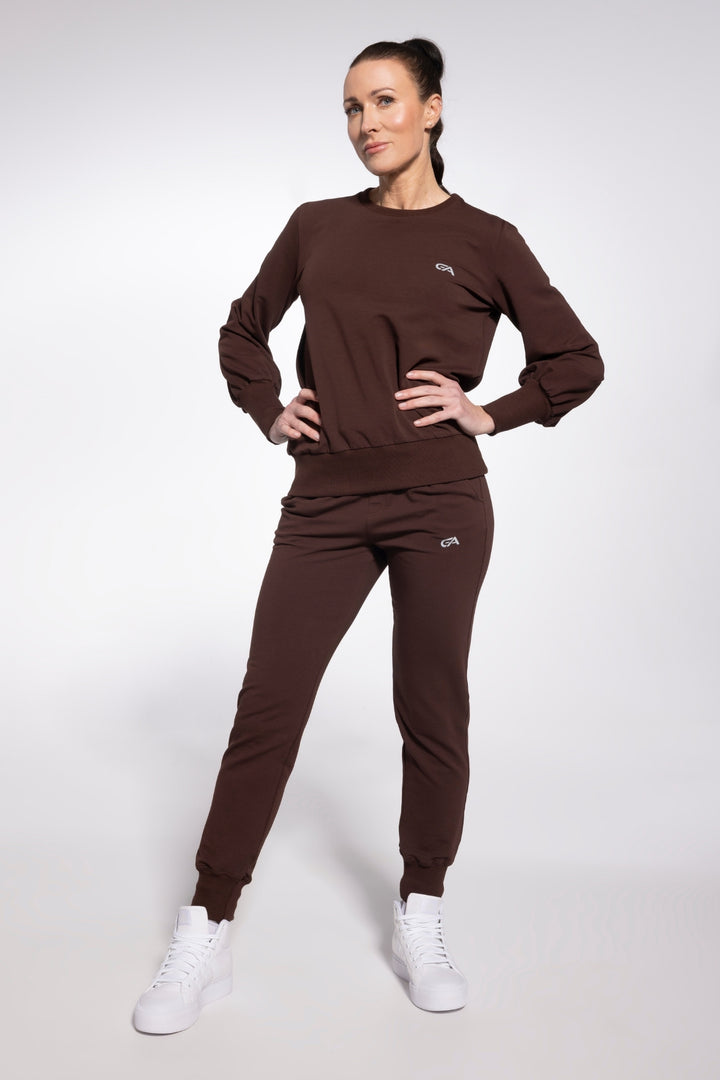 Woman wearing a brown tracksuit with white sneakers on a light gray background
