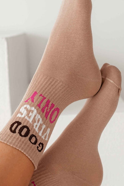 Close-up of beige cotton socks with "Good Vibes Only" slogan – bold lettering on soft fabric
