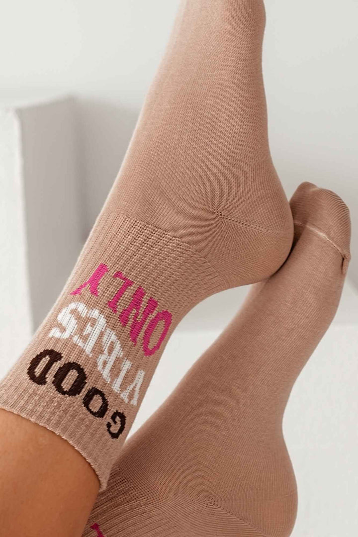 Close-up of beige cotton socks with "Good Vibes Only" slogan – bold lettering on soft fabric
