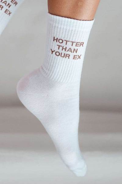 Close-up of white cotton socks with "Hotter Than Your Ex" slogan – bold lettering on soft fabric
