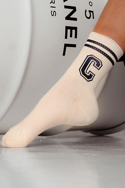 Close-up of white and ecru cotton socks with letter C – initial print detail on soft fabric
