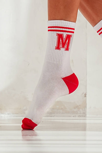 Close-up of white cotton socks with red letter M – bold initial print detail on soft fabric
