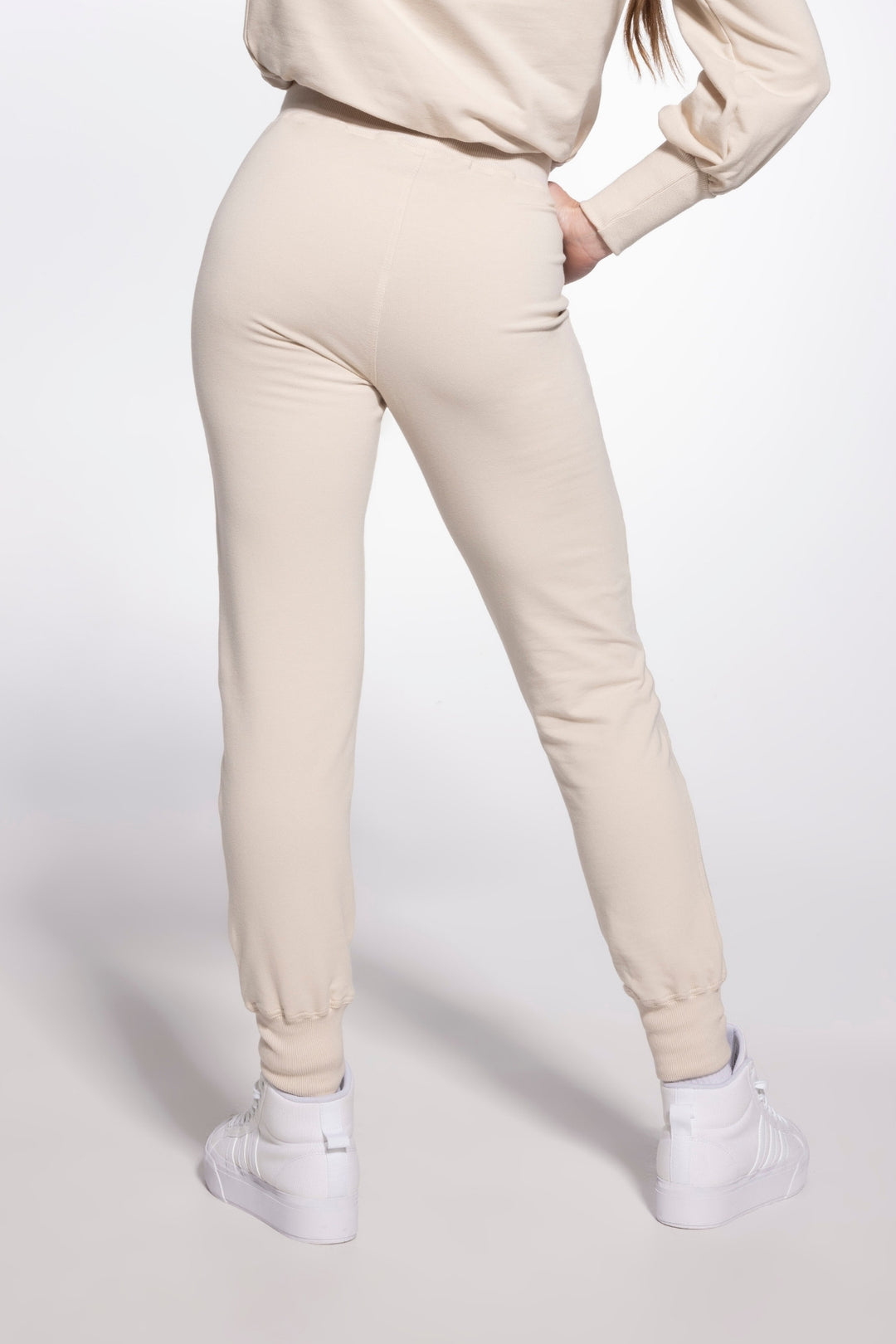 Person wearing beige jogger pants and a matching top on a white background