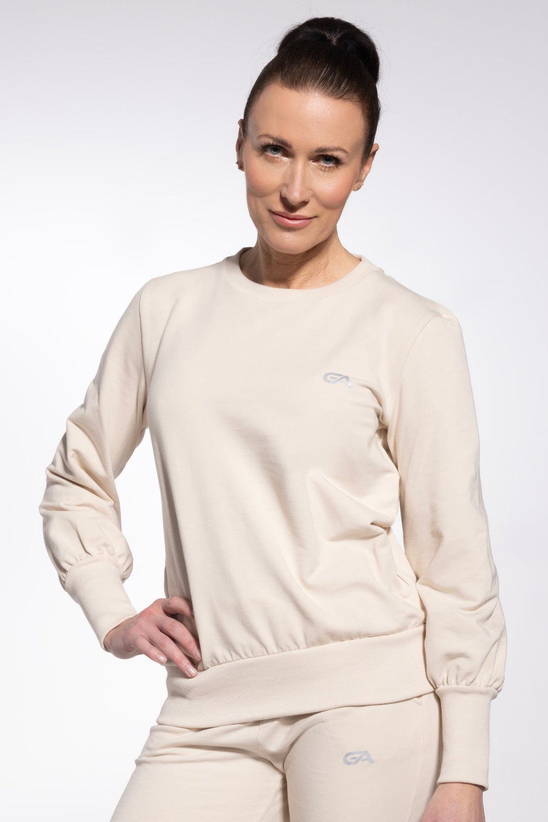 Woman wearing a beige sweatshirt and pants with a logo on a white background