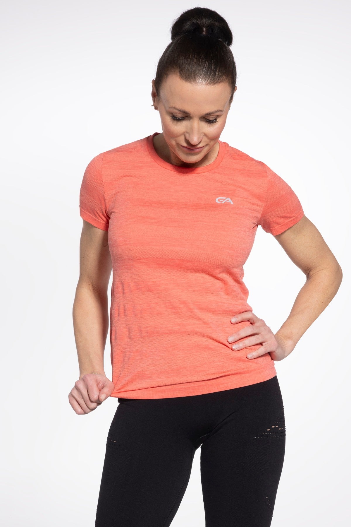 Woman wearing a coral athletic shirt and black leggings on a white background